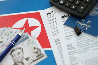 Kuzey Kore büyük miktarlarda para kazandı. Masada kalem, hesap makinesi, pasaport ve vergi formları var. Vergi ödeme ve muhasebe kavramı