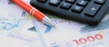 Arjantin pezosu. Büyük miktarda para. Masada, kalem ve hesap makinesi ile birlikte.