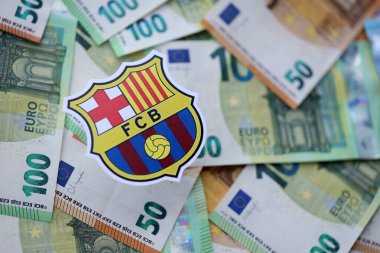 KYIV, UKRAINE - 23 Şubat 2025 FC Barcelona futbol kulübü rozeti büyük miktarda EURO para banknotlarının üzerinde yatıyor