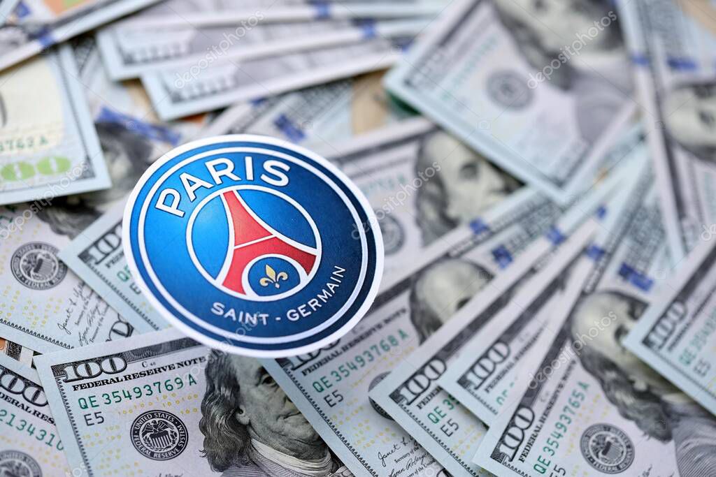 KYIV, UKRAINE - FEBRUARY 23, 2025 Paris Saint Germain FC football club badge lies on big amount of hundred US dollar bills