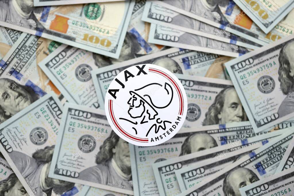 KYIV, UKRAINE - FEBRUARY 23, 2025 AFC Ajax football club badge lies on big amount of hundred US dollar bills