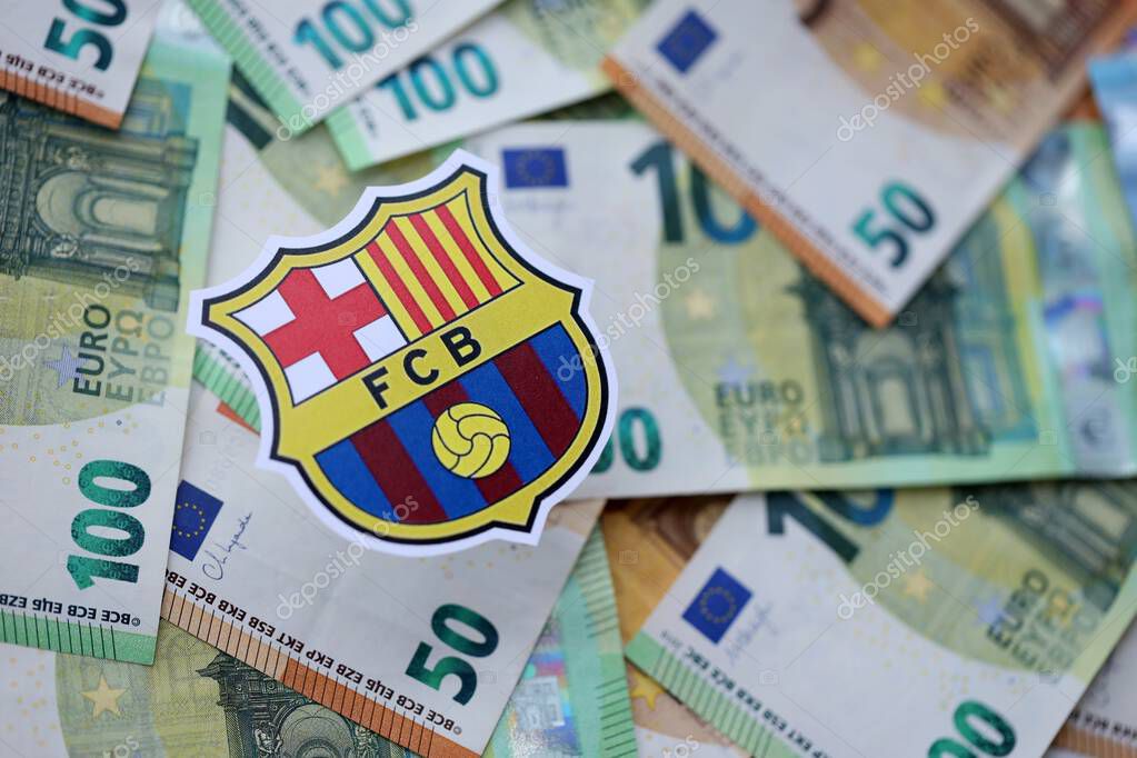 KYIV, UKRAINE - FEBRUARY 23, 2025 FC Barcelona football club badge lies on big amount of hundred EURO money bills