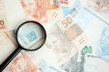 Brezilya reais banknotları ve büyüteç. Mevcut Brezilya gerçek para faturaları ve loupe büyük miktarda masada yatıyor. Brezilya 'da mali izleme ve vergilendirme kavramı