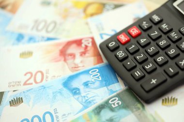 Israel New Shekels banknotları ve hesap makinesi. Mevcut İsrail para faturaları ve kalibreleri büyük miktarda masada yatıyor. İsrail 'de vergilendirme ve para kavramı