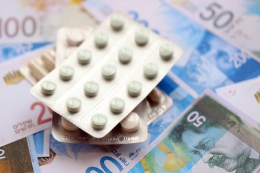 Israel New Shekels banknotları ve ilaç hapları. Mevcut İsrail para ve uyuşturucu faturaları büyük miktarda masada yatıyor. İsrail 'de ilaç ve eczane kavramı