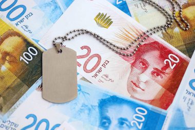 İsrail Yeni Şekelleri 'nin banknotları ve askeri simgesi. İsrail 'in mevcut para faturaları ve künyeleri büyük miktarda masada yatıyor. İsrail 'de askerlik kavramı