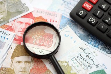 Pakistan banknotları ve büyüteçle hesap makinesi. Mevcut Pakistan para faturaları ve loupe ile calc büyük miktarda masada yatıyor. Pakistan 'da vergi ve para sayımı kavramı