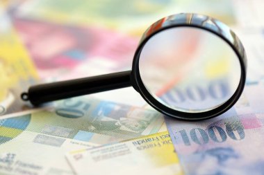 İsviçre frangı banknotları ve büyüteç. İçinde loupe olan şu anki para banknotları büyük miktarda masada yatıyor. İsviçre 'de mali izleme ve vergilendirme kavramı