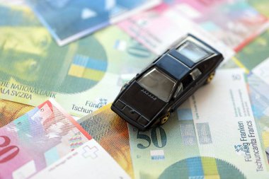 İsviçre frangı banknotları ve oyuncak araba. Mevcut frank, faturalar ve siyah araba büyük miktarda masada yatıyor. İsviçre 'de araba sahibi olma kavramı