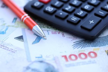 Arjantin Pezosu 'nun büyük miktarlarda para banknotları kalem ve hesap makinesiyle masanın üzerinde duruyor. Maliye ve vergi ödeme kavramı