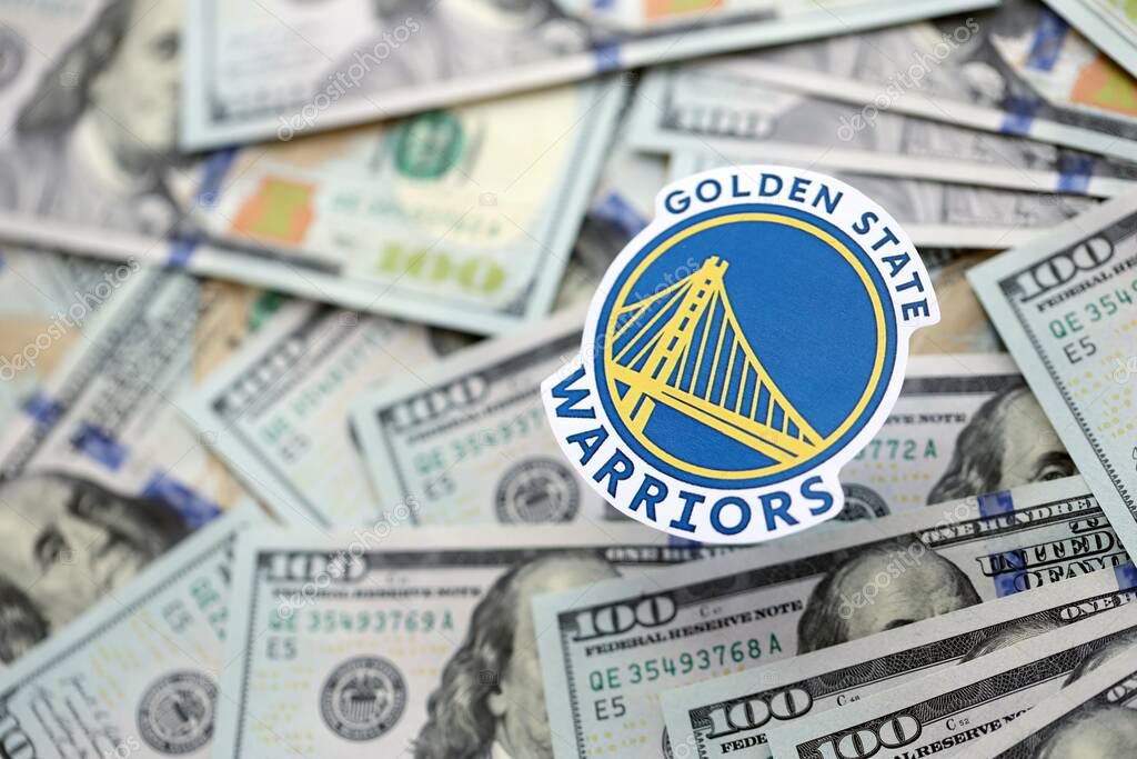 KYIV, UKRAINE - FEBRUARY 23, 2025 Golden State Warriors basketball team badge lies on big amount of hundred US dollar bills close up
