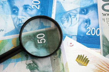 Israel New Shekels banknotları ve büyüteç. Şu anki İsrail 'in yüksek meblağlı faturaları masanın üzerinde yatıyor. İsrail 'de mali izleme ve vergilendirme kavramı