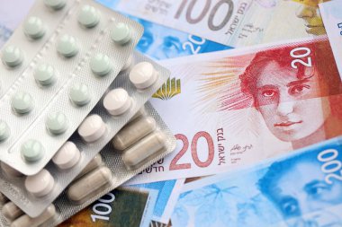 Israel New Shekels banknotları ve ilaç hapları. Mevcut İsrail para ve uyuşturucu faturaları büyük miktarda masada yatıyor. İsrail 'de ilaç ve eczane kavramı