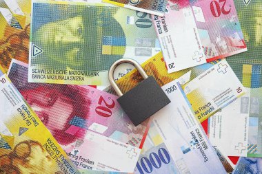 İsviçre frangı banknotları ve asma kilit. Mevcut para banknotları büyük miktarda masada yatıyor. İsviçre 'de yaptırımlar ve mali güvenlik kavramı