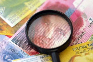 İsviçre frangı banknotları ve büyüteç. İçinde loupe olan şu anki para banknotları büyük miktarda masada yatıyor. İsviçre 'de mali izleme ve vergilendirme kavramı
