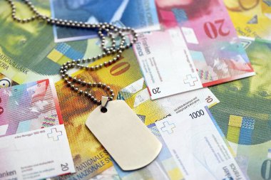 İsviçre frangı banknotları ve askeri jeton. Mevcut banknotlar ve künyeler masanın üzerinde büyük miktarda duruyor. İsviçre 'de askerlik konsepti