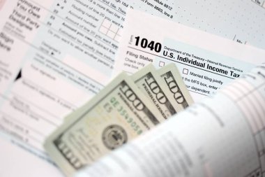 Yüz dolarlık banknotlar ve 1040 bireysel gelir vergisi iade formu yakın çekim. Çok az Amerikan doları ve Birleşik Devletler vergisi yok. ABD 'de vergi ödeme ve muhasebe kavramı