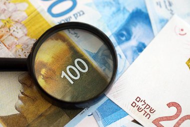 Israel New Shekels banknotları ve büyüteç. Şu anki İsrail 'in yüksek meblağlı faturaları masanın üzerinde yatıyor. İsrail 'de mali izleme ve vergilendirme kavramı