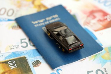 Israel New Shekels banknotları ve pasaportlu oyuncak araba. Geçerli İsrail para faturaları ve geçiş kartı olan siyah araba büyük miktarda masada yatıyor. İsrail 'de araba sahibi olma kavramı