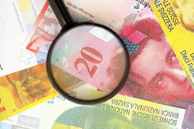 İsviçre frangı banknotları ve büyüteç. İçinde loupe olan şu anki para banknotları büyük miktarda masada yatıyor. İsviçre 'de mali izleme ve vergilendirme kavramı