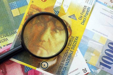 İsviçre frangı banknotları ve büyüteç. İçinde loupe olan şu anki para banknotları büyük miktarda masada yatıyor. İsviçre 'de mali izleme ve vergilendirme kavramı