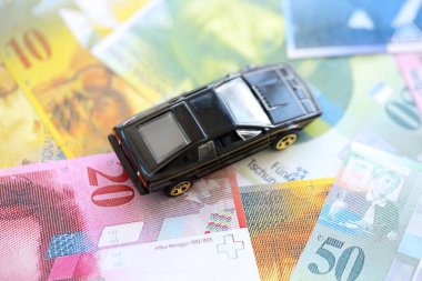 İsviçre frangı banknotları ve oyuncak araba. Mevcut frank, faturalar ve siyah araba büyük miktarda masada yatıyor. İsviçre 'de araba sahibi olma kavramı
