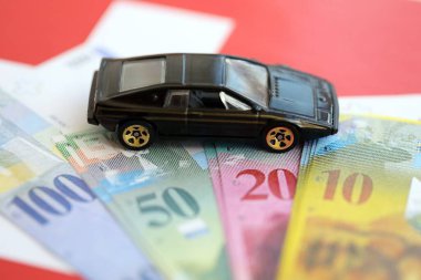 İsviçre frangı banknotları ve bayrak üstünde oyuncak araba. Mevcut frank, faturalar ve siyah araba bayrağın üzerinde duruyor. İsviçre 'de araba sahibi olma kavramı