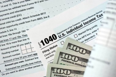 Yüz dolarlık banknotlar ve 1040 bireysel gelir vergisi iade formu yakın çekim. Çok az Amerikan doları ve Birleşik Devletler vergisi yok. ABD 'de vergi ödeme ve muhasebe kavramı