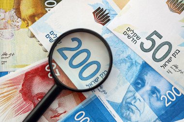 Israel New Shekels banknotları ve büyüteç. Şu anki İsrail 'in yüksek meblağlı faturaları masanın üzerinde yatıyor. İsrail 'de mali izleme ve vergilendirme kavramı