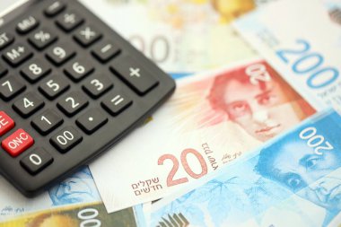 Israel New Shekels banknotları ve hesap makinesi. Mevcut İsrail para faturaları ve kalibreleri büyük miktarda masada yatıyor. İsrail 'de vergilendirme ve para kavramı