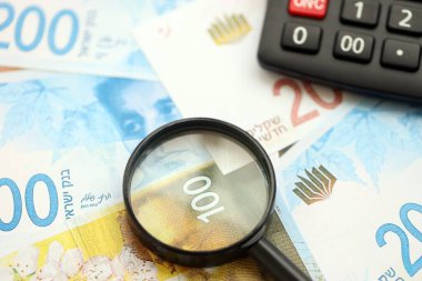 Israel New Shekels banknotları ve büyüteçle birlikte hesap makinesi. Mevcut İsrail para faturaları ve loupe ile calc büyük miktarda masada yatıyor. İsrail 'de vergilendirme ve para kavramı
