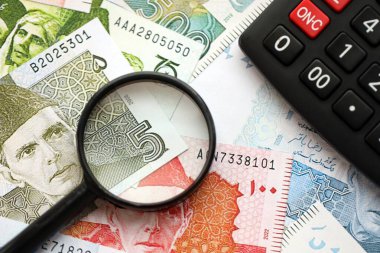 Pakistan banknotları ve büyüteçle hesap makinesi. Mevcut Pakistan para faturaları ve loupe ile calc büyük miktarda masada yatıyor. Pakistan 'da vergi ve para sayımı kavramı