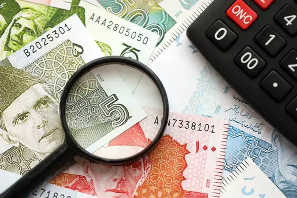 Pakistan banknotları ve büyüteçle hesap makinesi. Mevcut Pakistan para faturaları ve loupe ile calc büyük miktarda masada yatıyor. Pakistan 'da vergi ve para sayımı kavramı