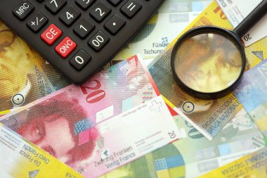 İsviçre frangı banknotları ve büyüteçli hesap makinesi. Mevcut para faturaları ve loupe ile calc büyük miktarda masada yatıyor. İsviçre 'de vergilendirme ve iş kavramı