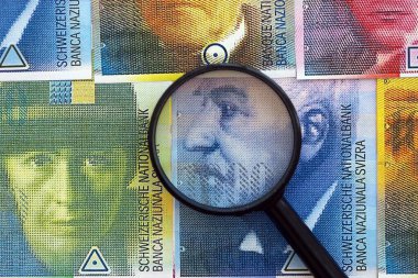 İsviçre frangı banknotları ve büyüteç. Loupe 'un para faturaları büyük miktarda masada duruyor. İsviçre 'de mali izleme ve vergilendirme kavramı