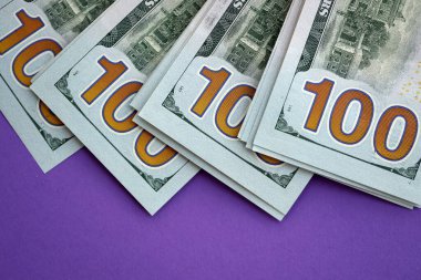 Mor arka planda büyük miktarda yüz dolarlık banknotlar. ABD 'de vergilendirme ve para yapma kavramı