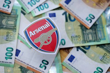 KYIV, UKRAINE - 23 Şubat 2025 Arsenal FC futbol kulübü rozeti büyük miktarda EURO para banknotlarının üzerinde yatıyor
