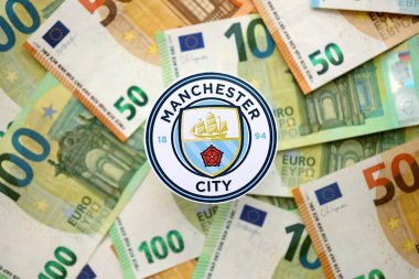 KYIV, UKRAINE - 23 Şubat 2025 Manchester City FC futbol kulübü rozeti büyük miktarda EURO para banknotlarının üzerinde yatıyor