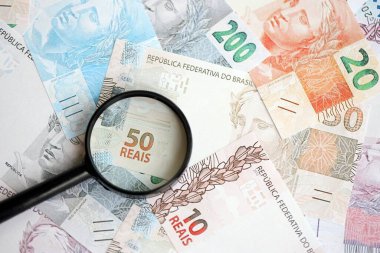 Brezilya reais banknotları ve büyüteç. Mevcut Brezilya gerçek para faturaları ve loupe büyük miktarda masada yatıyor. Brezilya 'da mali izleme ve vergilendirme kavramı