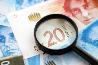 Israel New Shekels banknotları ve büyüteç. Şu anki İsrail 'in yüksek meblağlı faturaları masanın üzerinde yatıyor. İsrail 'de mali izleme ve vergilendirme kavramı