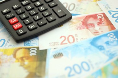 Israel New Shekels banknotları ve hesap makinesi. Mevcut İsrail para faturaları ve kalibreleri büyük miktarda masada yatıyor. İsrail 'de vergilendirme ve para kavramı