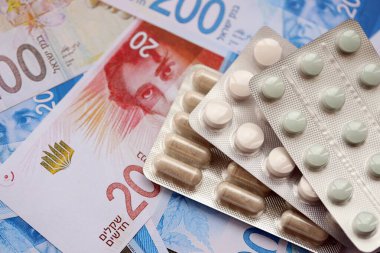 Israel New Shekels banknotları ve ilaç hapları. Mevcut İsrail para ve uyuşturucu faturaları büyük miktarda masada yatıyor. İsrail 'de ilaç ve eczane kavramı