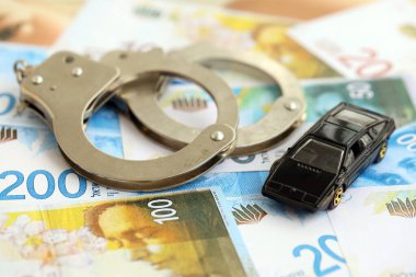 Israel New Shekels banknotları ve kelepçeli oyuncak araba. Şu anki İsrail para faturaları ve kelepçeli siyah araba büyük miktarda masada yatıyor. İsrail 'de araba kazası kavramı