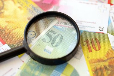 İsviçre frangı banknotları ve büyüteç. İçinde loupe olan şu anki para banknotları büyük miktarda masada yatıyor. İsviçre 'de mali izleme ve vergilendirme kavramı