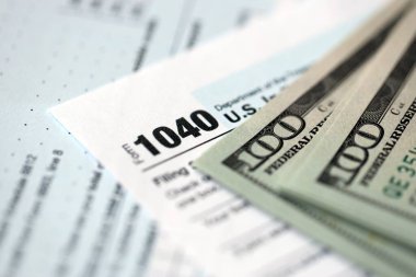 Yüz dolarlık banknotlar ve 1040 bireysel gelir vergisi iade formu yakın çekim. Çok az Amerikan doları ve Birleşik Devletler vergisi yok. ABD 'de vergi ödeme ve muhasebe kavramı