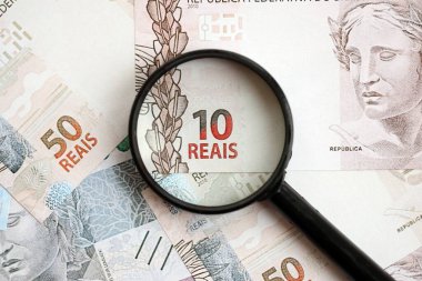 Brezilya reais banknotları ve büyüteç. Mevcut Brezilya gerçek para faturaları ve loupe büyük miktarda masada yatıyor. Brezilya 'da mali izleme ve vergilendirme kavramı