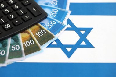 Israel New Shekels banknotları ve hesap makinesi bayrağın üzerinde. İsrail 'in mevcut para faturaları ve kalibreleri büyük oranda bayrakta yatıyor. İsrail 'de vergilendirme ve para kavramı