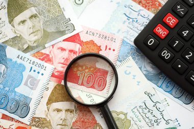 Pakistan banknotları ve büyüteçle hesap makinesi. Mevcut Pakistan para faturaları ve loupe ile calc büyük miktarda masada yatıyor. Pakistan 'da vergi ve para sayımı kavramı
