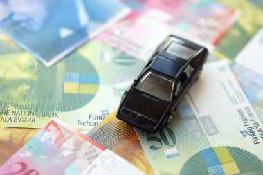 İsviçre frangı banknotları ve oyuncak araba. Mevcut frank, faturalar ve siyah araba büyük miktarda masada yatıyor. İsviçre 'de araba sahibi olma kavramı