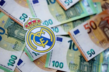 KYIV, UKRAINE - 23 Şubat 2025 Real Madrid CF futbol kulübü rozeti büyük miktarda EURO para banknotlarının üzerinde yatıyor